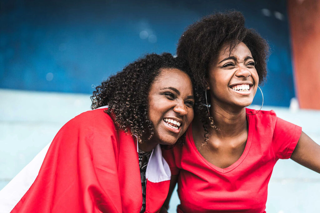 Dos mujeres afroperuanas sonrientes, una envuelta en una bandera del Perú, celebrando en un espacio público