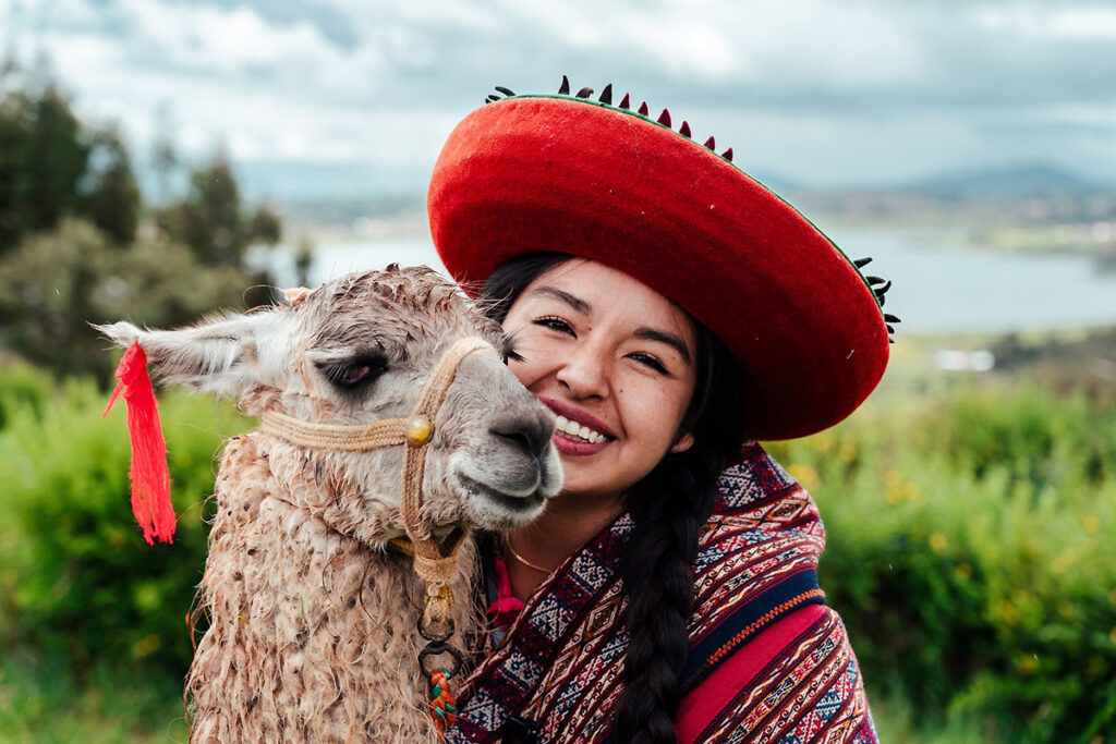 Mujer andina con vestimenta tradicional sonriendo junto a una llama en los Andes peruanos