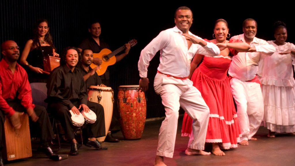 Grupo de músicos y bailarines afroperuanos en escenario, interpretando música y danza tradicional con cajón, bongós y guitarra