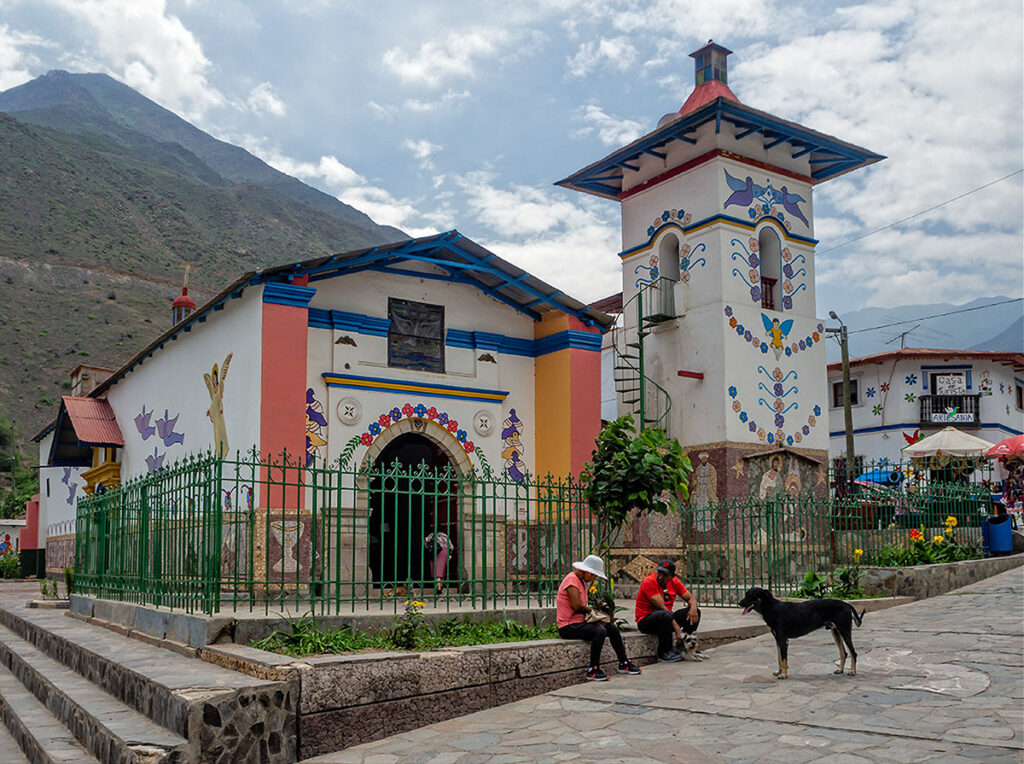 Iglesia de Santiago Apóstol en Antioquía decorada con arte naïf, con cerros al fondo y vecinos en la plaza