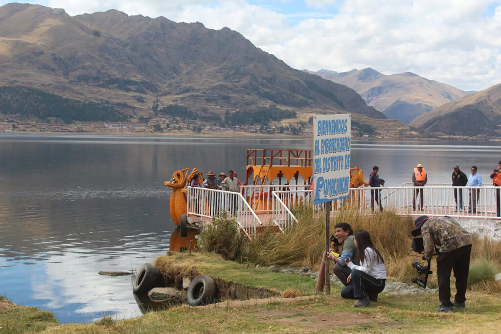 Embarcadero rústico con cartel de bienvenida en la laguna Pomacanchi, rodeado de montañas y visitantes locales