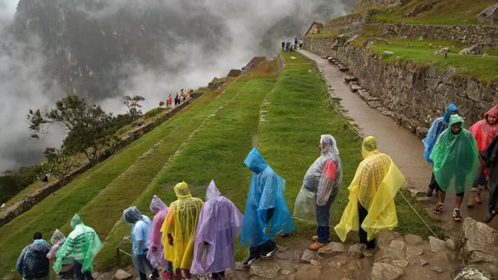 turistas con ponchos caminando por senderos de Machu Picchu en temporada de lluvias
