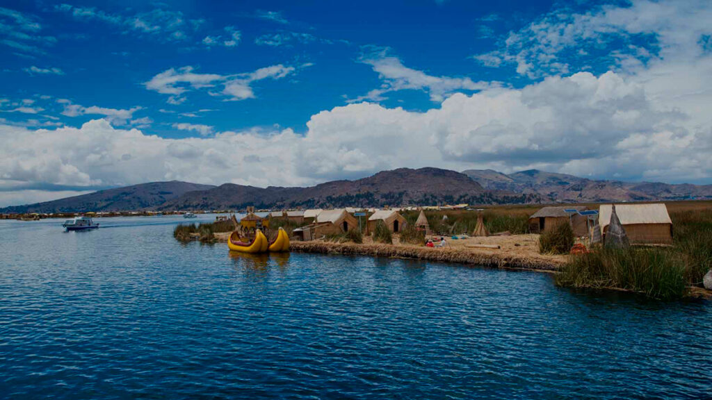 Vista del Lago Titicaca con balsas de totora, orillas pobladas y el altiplano al fondo en un día despejado