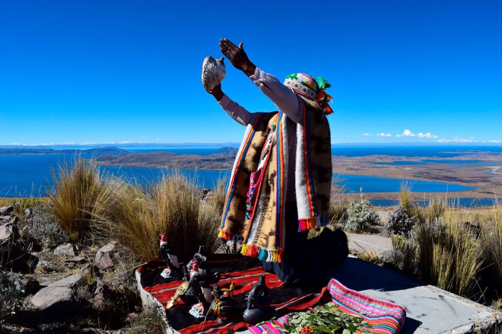 Comunero de Amantaní realiza un gesto ritual frente al lago Titicaca, con ofrendas extendidas en un manto tradicional