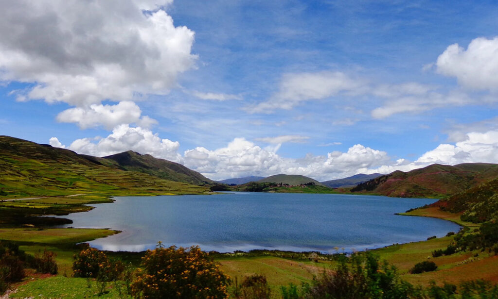 Laguna altoandina en Cusco bajo un cielo parcialmente nublado, con cerros y campos alrededor