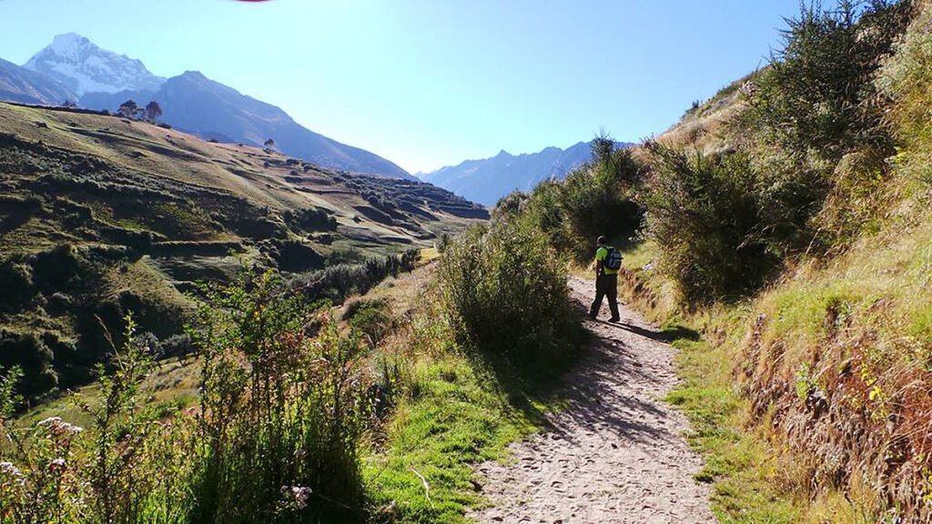 senderista caminando por un sendero en Pitec con montañas al fondo