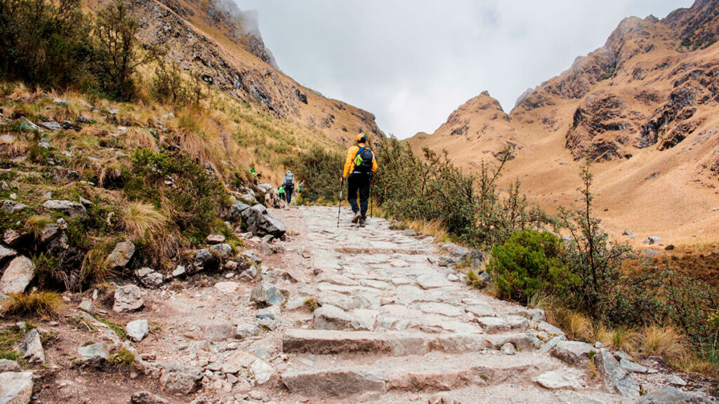 Tramo del camino inca, también conocido como Qhapaq Ñan en los Andes peruanos, camino empedrado rodeado de montañas, con viajeros recorriendo la histórica red vial inca