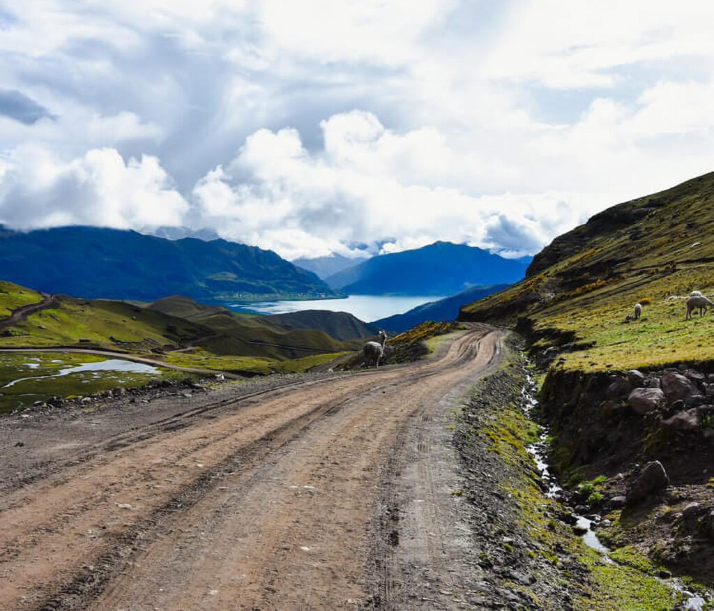 Camino afirmado en el altiplano cusqueño, con vista a una laguna y cerros andinos