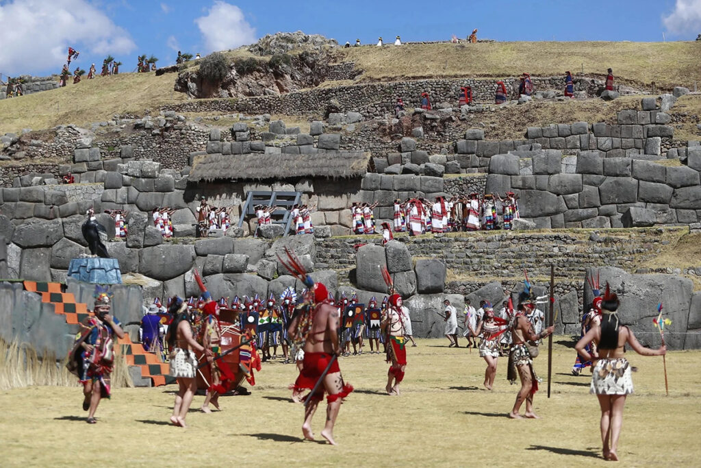 Vista de Sacsayhuamán en Cusco con muros de piedra en zigzag y recreación ceremonial andina, mostrando la magnitud de la fortaleza inca