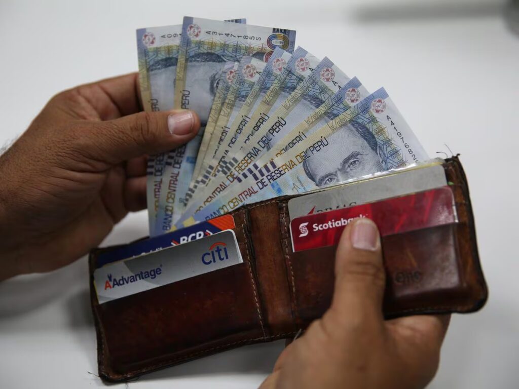 Persona sosteniendo billetes de soles peruanos junto a tarjetas bancarias en una billetera