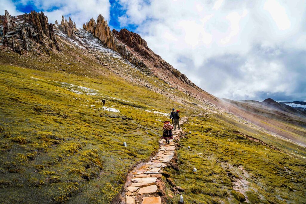 Turistas caminando por el sendero de Palccoyo, rodeados de montañas andinas y formaciones rocosas en el camino hacia la montaña de colores