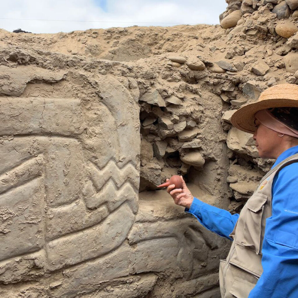 rqueóloga examina los relieves del mural 3D en la Huaca Yolanda, con figuras geométricas y símbolos de la cosmovisión prehispánica