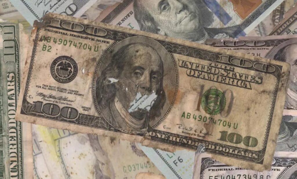 Billete de cien dólares deteriorado entre otros billetes en mejor estado
