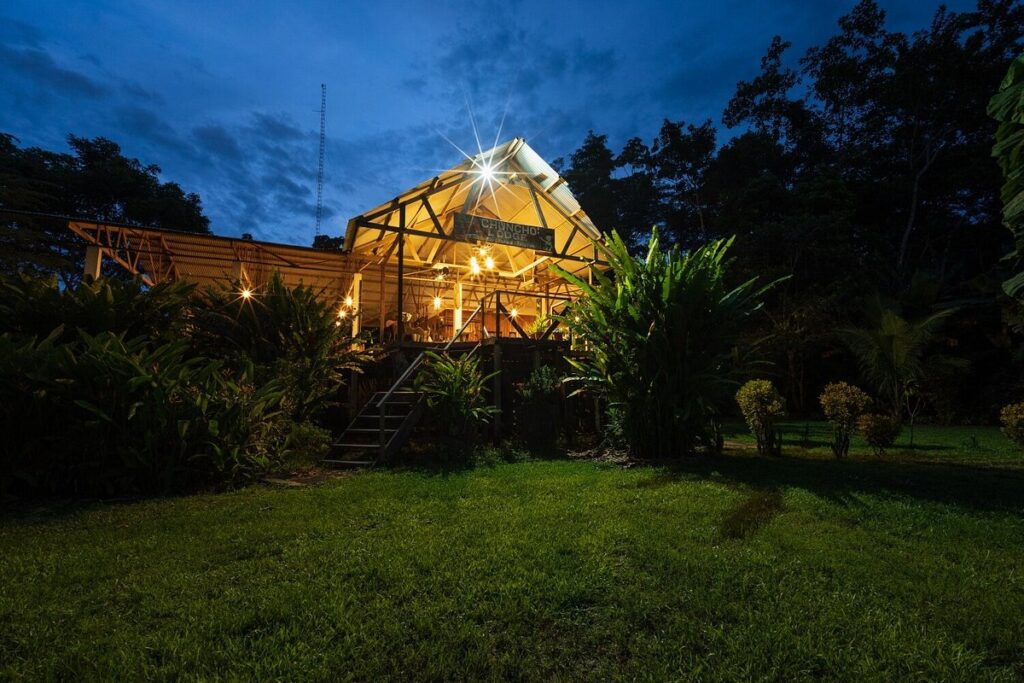 Lodge amazónico en Tambopata iluminado de noche rodeado de vegetación selvática