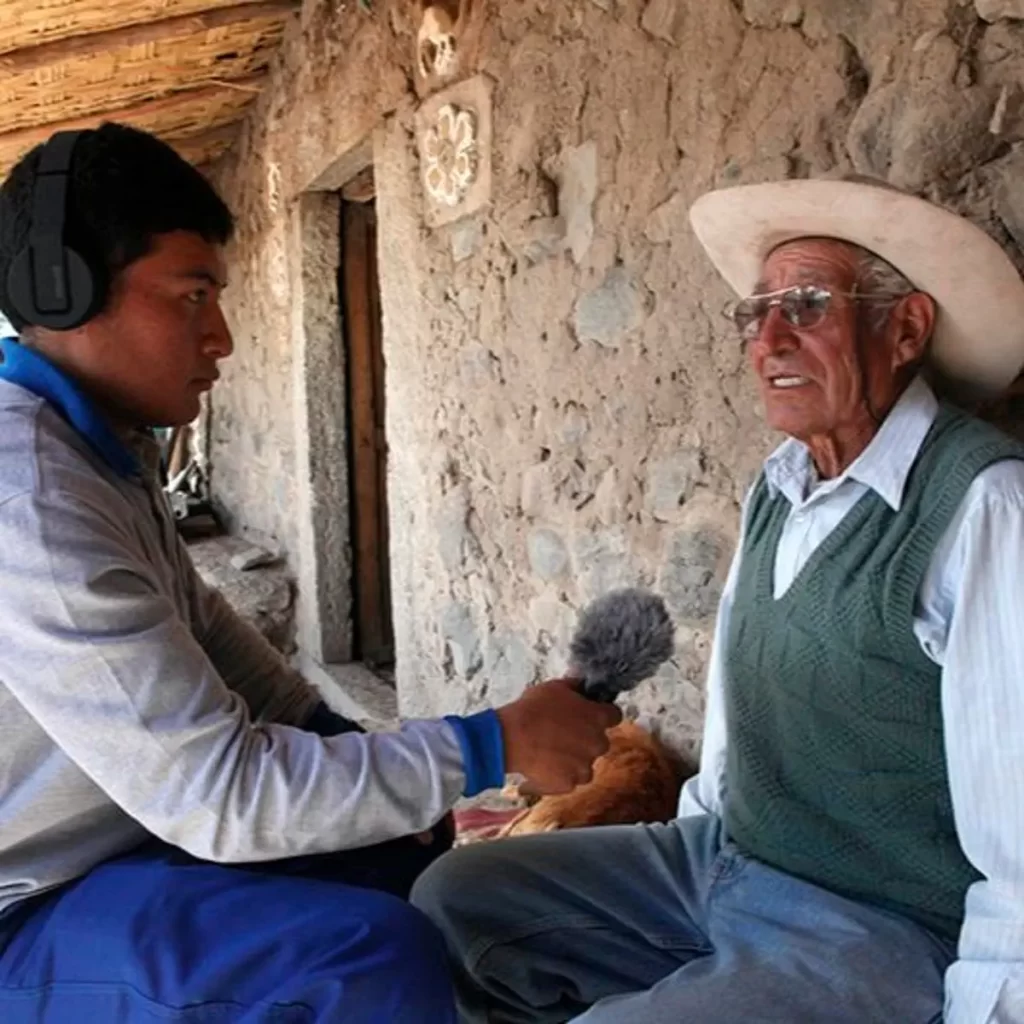 Joven entrevistando en quechua a un hombre mayor en una comunidad andina, ejemplo de proyectos digitales y radiales que difunden la lengua