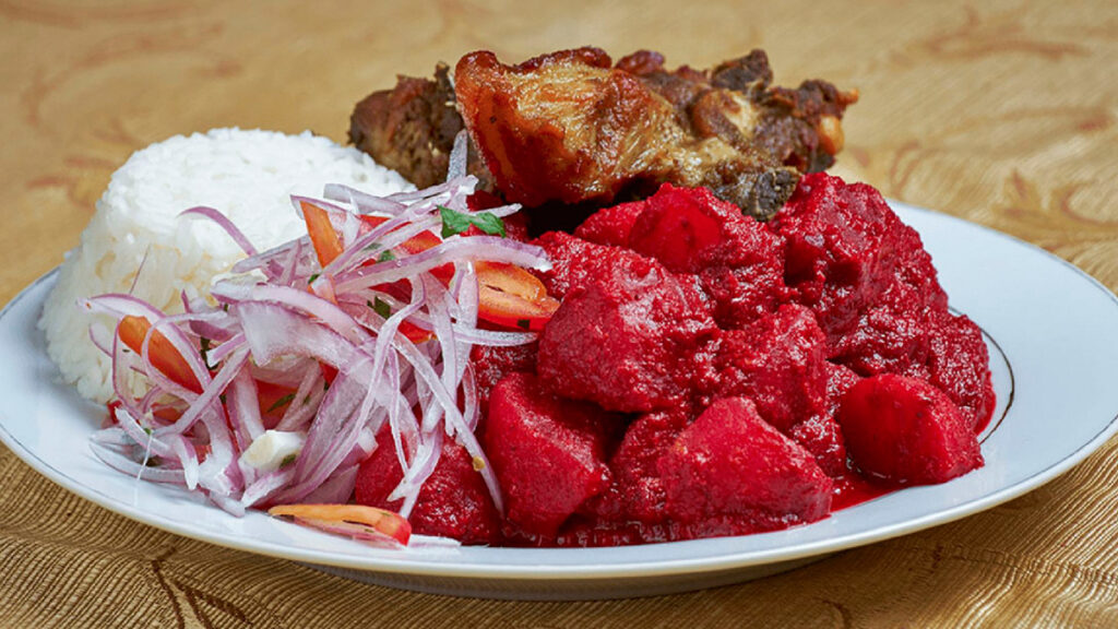 Guiso tradicional ayacuchano de papas bañadas en salsa roja de maní y betarraga, acompañado de arroz blanco, carne frita y ensalada criolla con cebolla morada y ajíes.