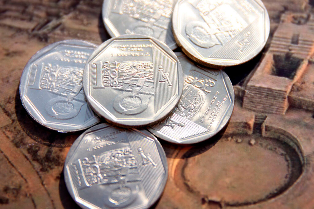 Monedas de un sol peruano sobre superficie con diseño arqueológico