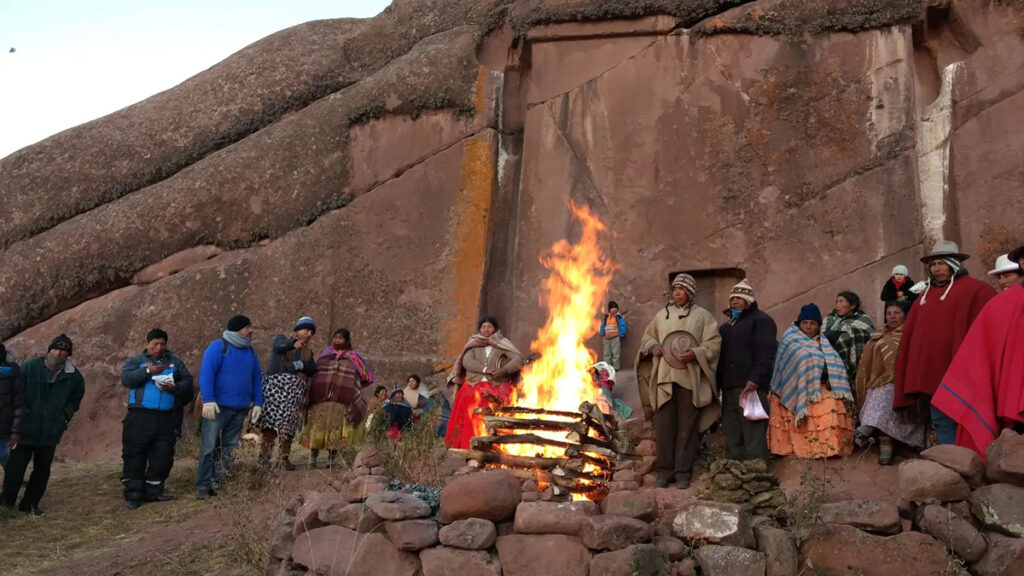 Ceremonia andina frente al portal de Aramu Muru con fuego ritual y participantes vestidos con atuendos tradicionales