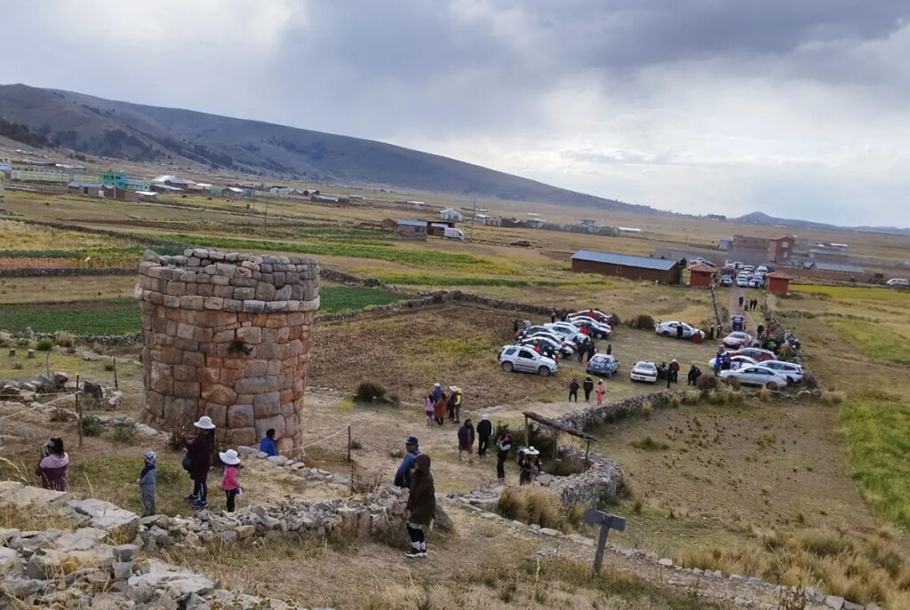 Vista del conjunto funerario de Molloco en Ácora, Puno, con chullpas de piedra labrada sobre una ladera andina y visitantes recorriendo el sitio