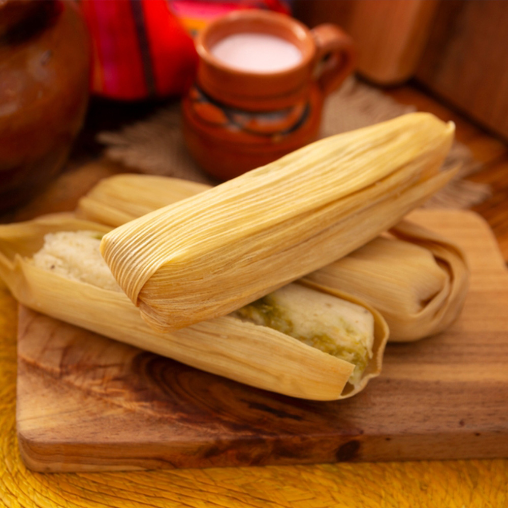Tamal cuzqueño envuelto en hojas de maíz sobre tabla de madera, acompañado de taza de chicha y textiles andinos, elaborado con maíz blanco del Valle Sagrado