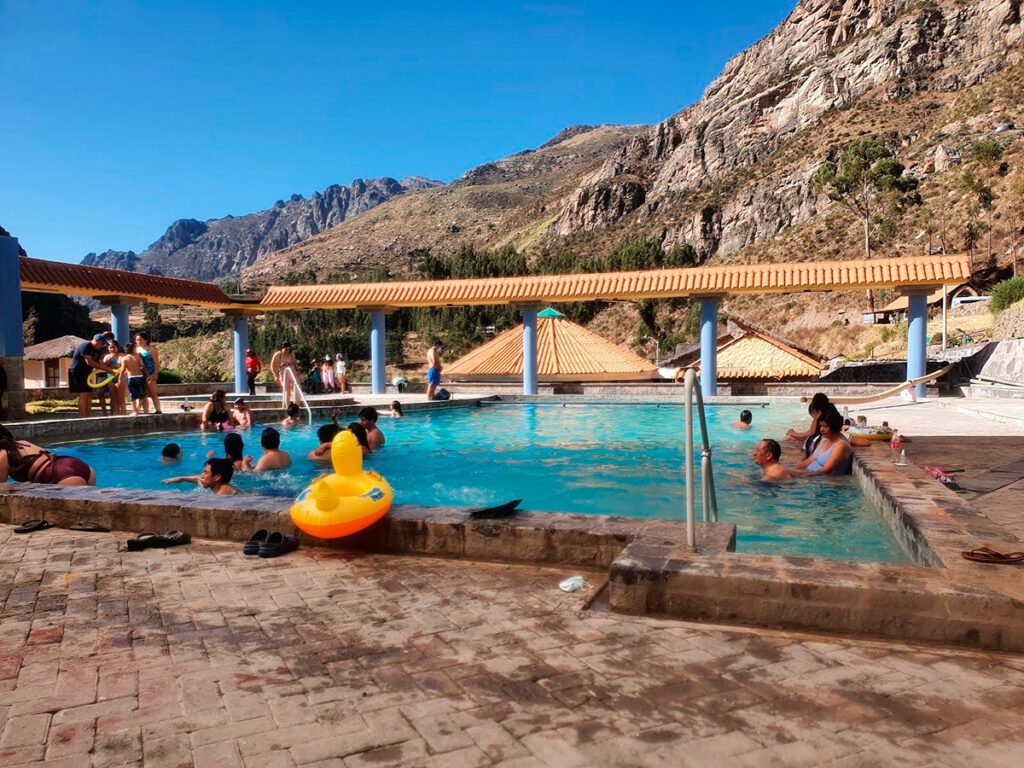 Visitantes disfrutando de las piscinas termales de La Calera en Chivay, rodeadas por montañas del valle del Colca bajo el cielo azul