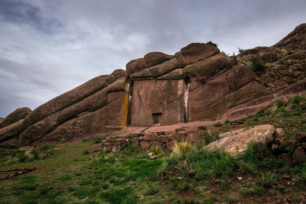 Vista panorámica del portal de Aramu Muru tallado en la roca rojiza del altiplano, rodeado de montañas y vegetación andina