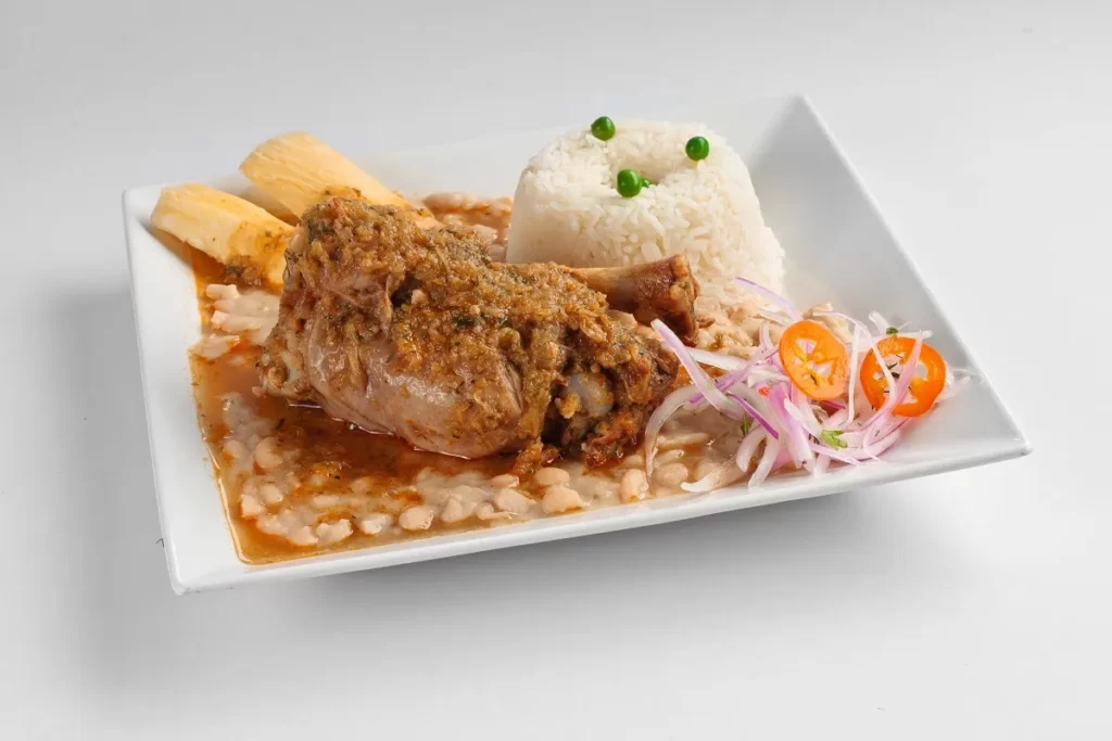 Seco de cabrito con arroz, frejoles y sarza criolla, preparado con zapallo loche y culantro fresco, un plato emblemático de la cocina tradicional de Lambayeque