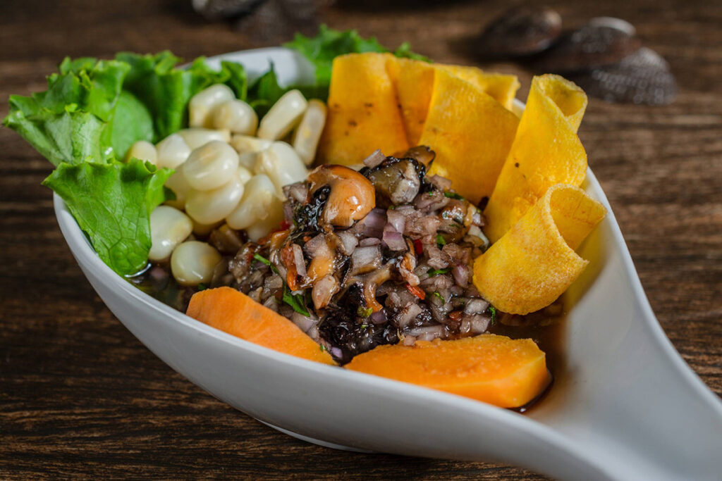 Ceviche de conchas negras servido con plátano frito, camote y maíz, un plato tradicional de los manglares de Tumbes que resalta los sabores del norte del Perú