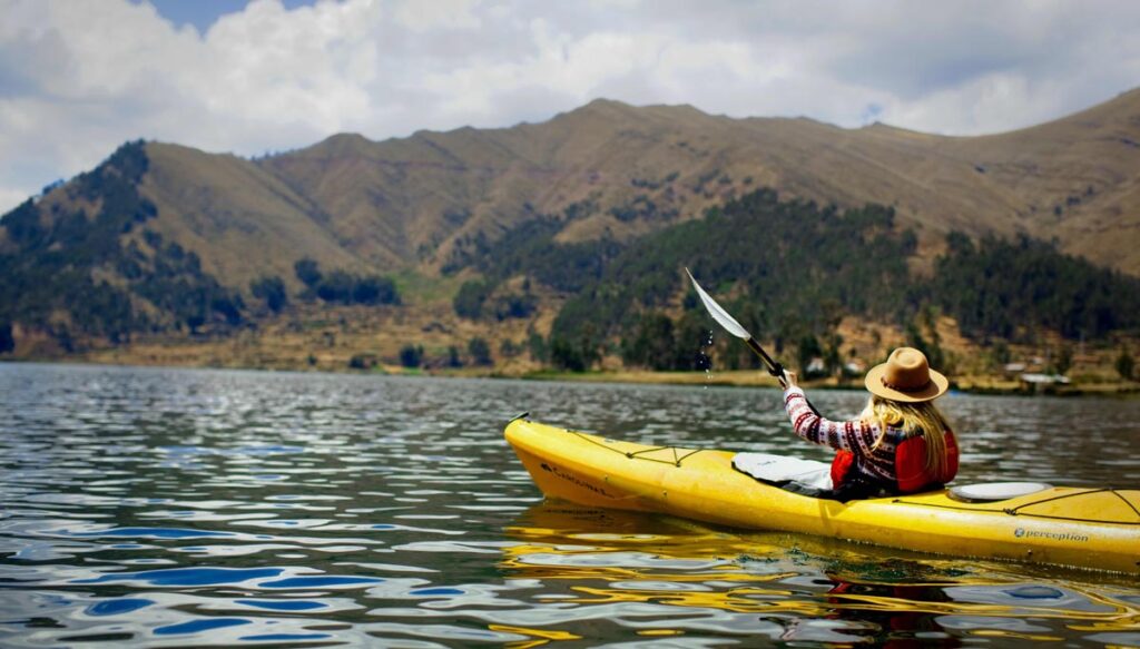 Visitante practicando kayak en la laguna Piuray rodeada de colinas agrícolas y montañas del Valle Sagrado del Cusco