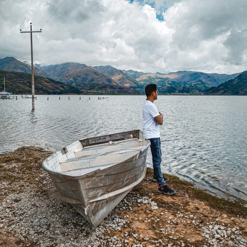 Persona junto a una embarcación en la orilla de la Laguna de Piuray, con los Andes de Cusco al fondo