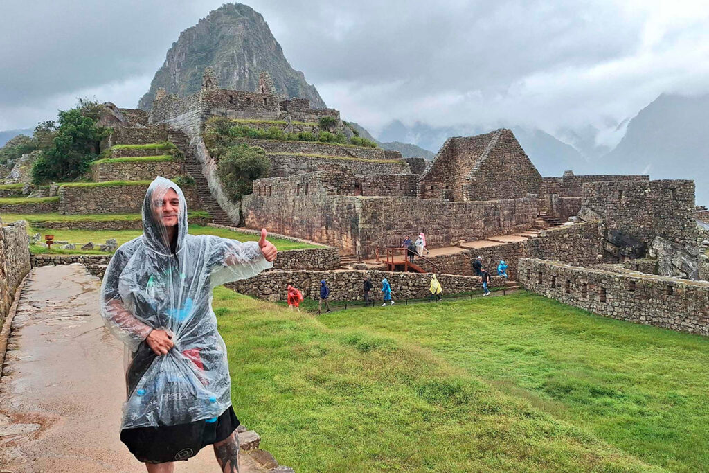 Turista con poncho impermeable frente a Machu Picchu durante un día lluvioso en la temporada de lluvias en Cusco, Perú