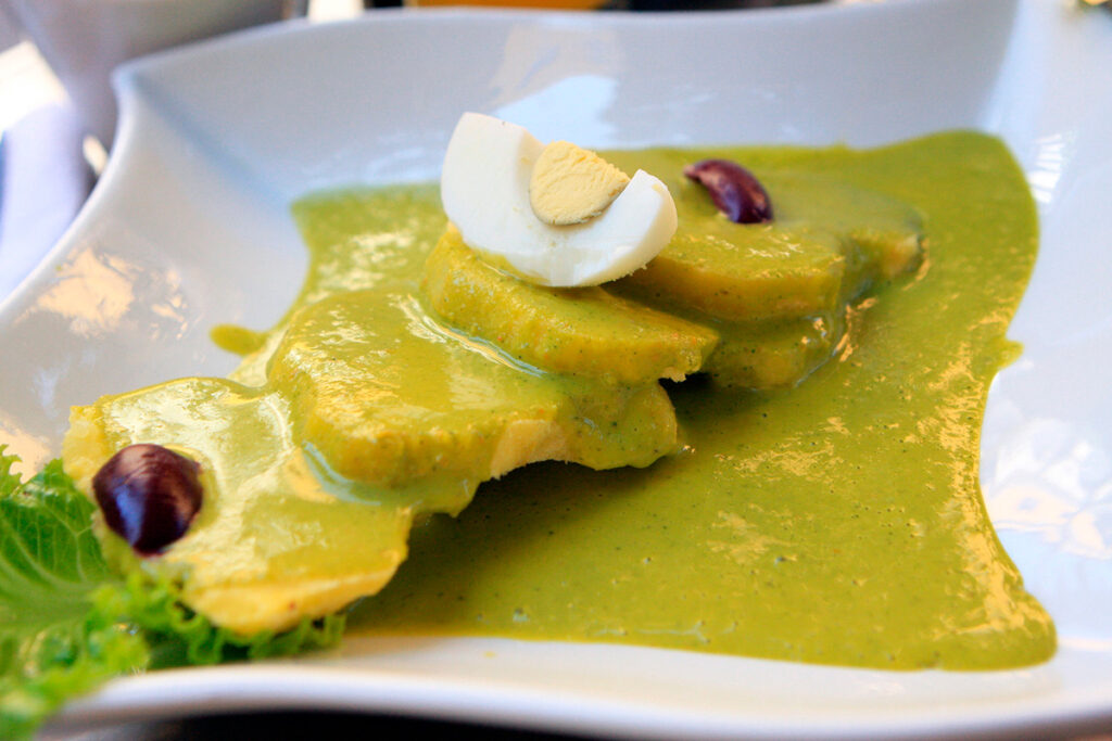Plato de ocopa arequipeña servido sobre papas sancochadas, cubiertas con salsa de huacatay y maní, acompañado de huevo duro y aceitunas