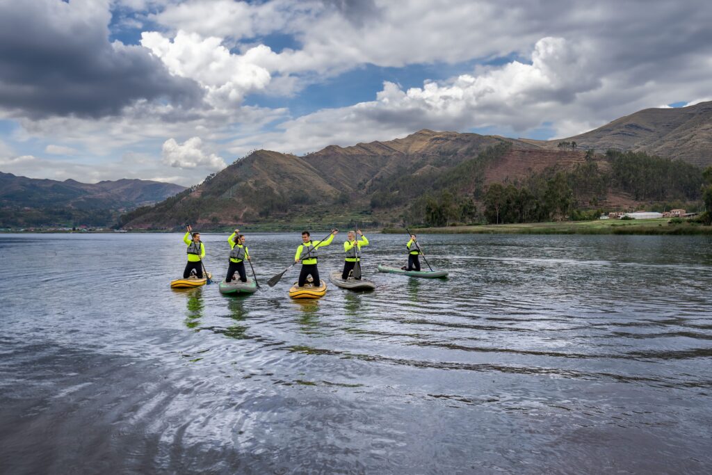 Grupo de turistas practicando stand-up paddle en la Laguna de Piuray, rodeada por montañas del Valle Sagrado de Cusco, Perú
