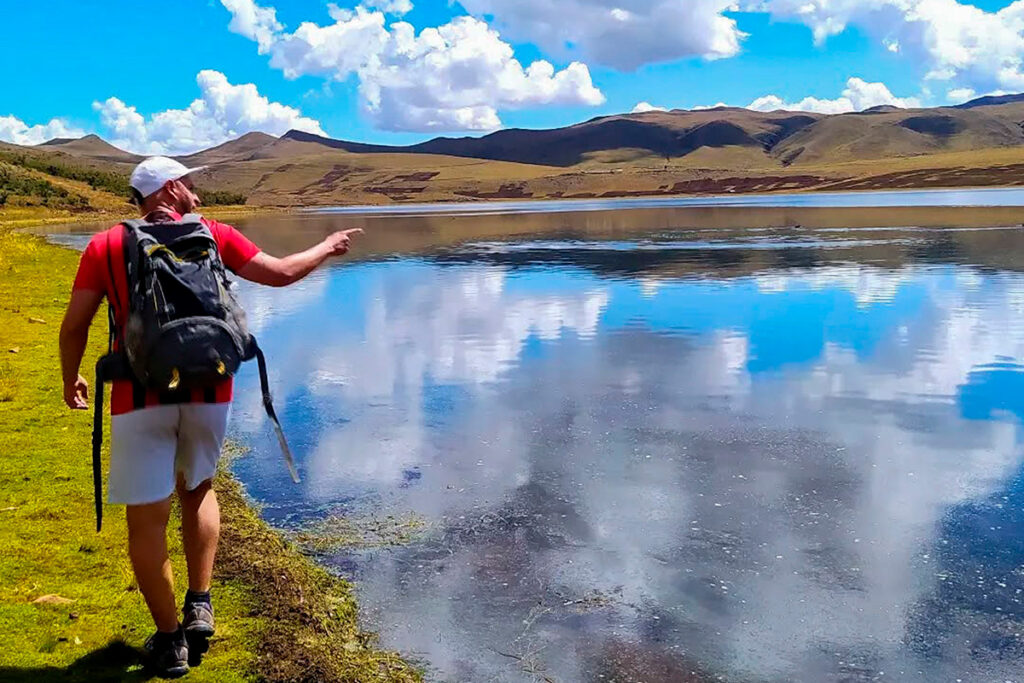 Viajero realizando trekking junto a la laguna de Qoricocha en Cusco, rodeado de montañas y reflejos del cielo andino