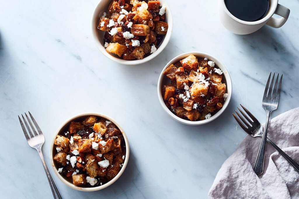 Tazones de ranfañote con pan frito, frutos secos y coco rallado, acompañados de tazas de café sobre mesa de mármol