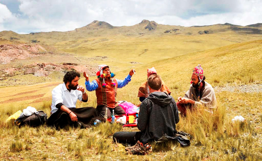 guía andino realizando ceremonia espiritual con viajeros en los Andes del Cusco, rodeados de montañas y paisajes sagrados