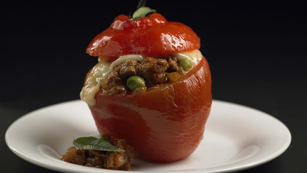 Rocoto relleno arequipeño servido en plato blanco, con ají rojo relleno de carne sazonada, arvejas y queso gratinado, acompañado de guarnición