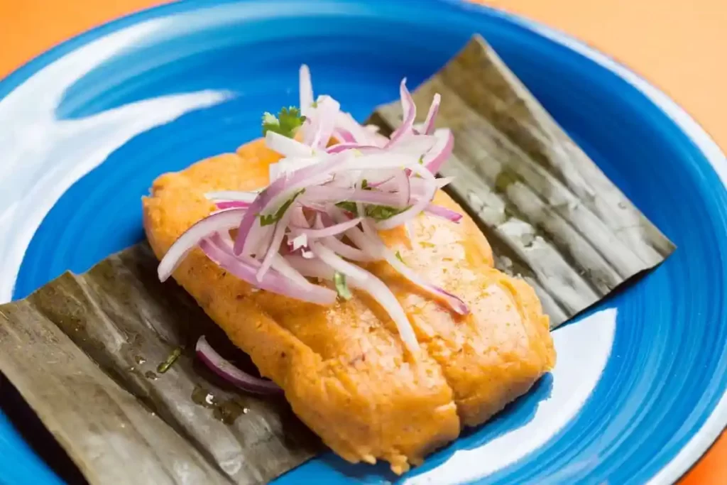 Tamal limeño servido sobre hoja de plátano, acompañado de cebolla roja y presentado en plato azul, un clásico de la cocina tradicional del centro histórico de Lima