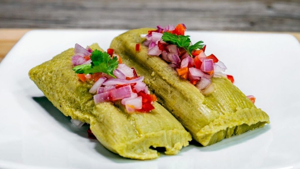 Tamal verde norteño servido con salsa criolla sobre plato blanco, elaborado con choclo y culantro, un clásico desayuno tradicional de Piura y Lambayeque