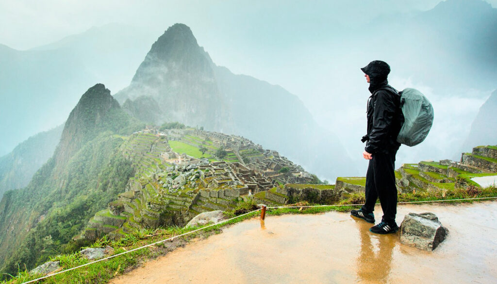 Viajero con impermeable observando Machu Picchu bajo la neblina durante la temporada de lluvias en Cusco, Perú