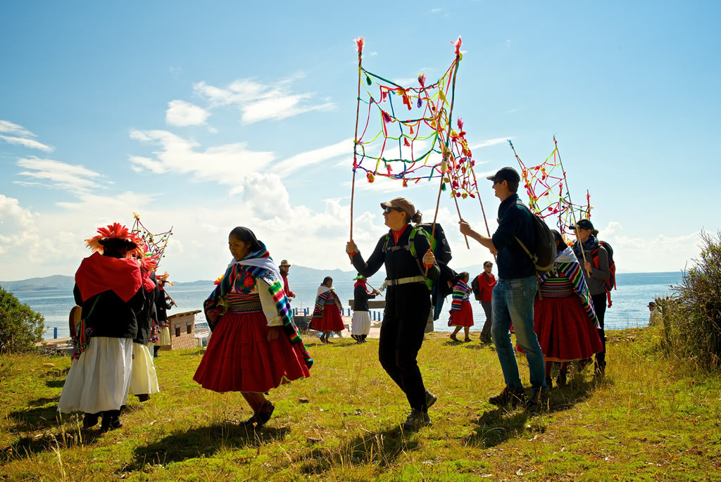 viajeros participando en una ceremonia andina frente al lago Titicaca, guiados por pobladores locales con trajes tradicionales
