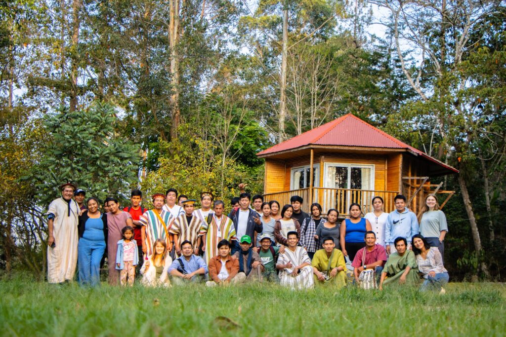Grupo de comuneros yánesha junto a una casa de madera en la selva central del Perú, símbolo de hospitalidad y participación en experiencias de turismo vivencial en Oxapampa