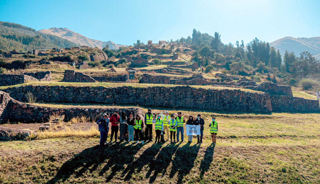 Grupo de visitantes en el sitio arqueológico de Raqayraqayniyuq, Cusco, frente a los andenes incas restaurados del valle andino