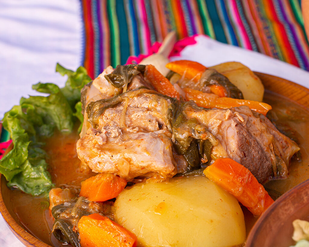 Adobo Ayacuchano con carne de cerdo, papas y verduras, servido en plato de barro sobre mantel andino tradicional