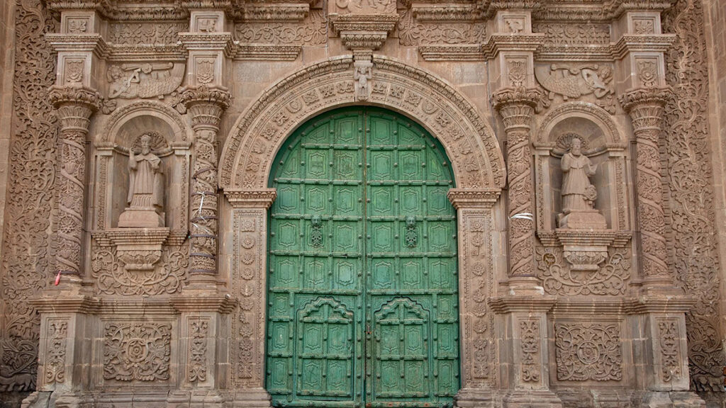 Detalle de la portada de la Catedral de Puno con relieves tallados y puerta verde central, ejemplo del arte simbólico del barroco andino