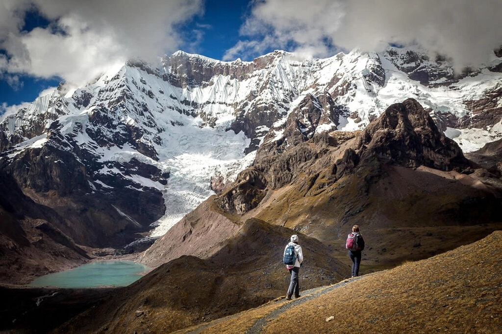 Caminantes recorren los senderos del Ausangate frente a una laguna glaciar en el sur andino del Cusco