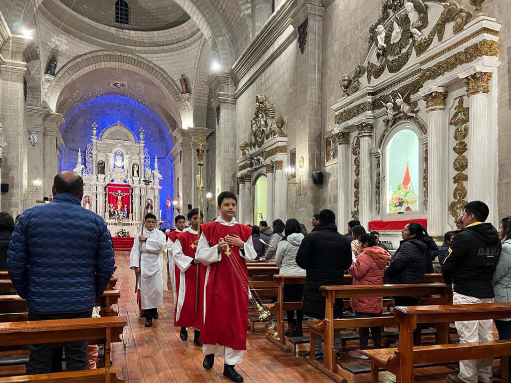 Interior de la Catedral de Puno durante una misa, con feligreses y acólitos vestidos de rojo participando en una celebración religiosa