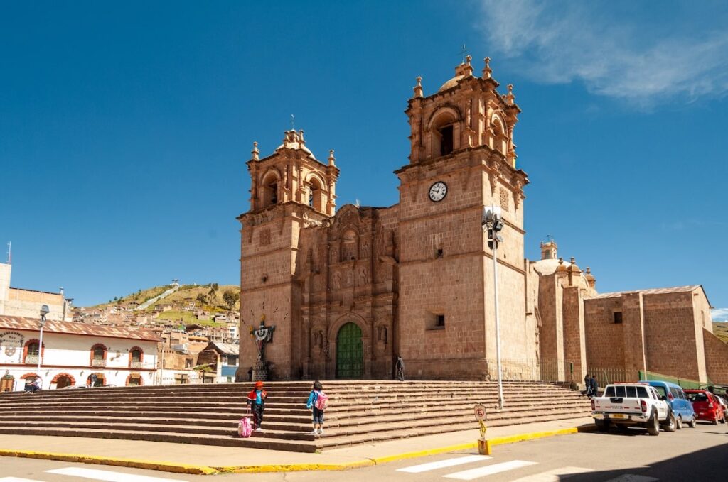 Vista frontal de la Catedral de Puno bajo el cielo azul del altiplano, con su fachada barroca andina y escalinatas de acceso desde la Plaza Mayor