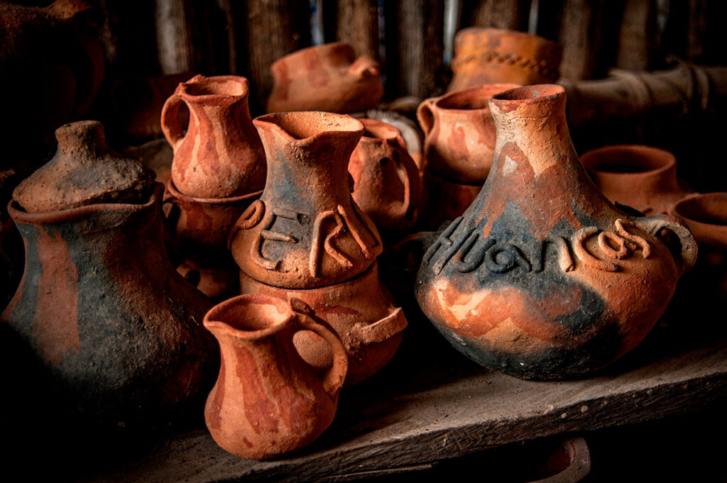 Conjunto de cántaros y jarras de cerámica de Huancas en tonos rojizos y oscuros, dispuestos sobre una superficie de madera dentro de un taller tradicional