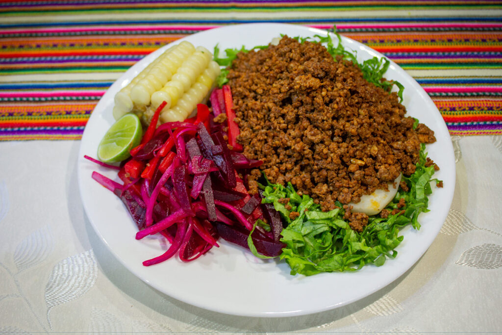 Plato tradicional de Chorizo Ayacuchano acompañado de ensalada de beterraga y maíz sancochado sobre mantel andino